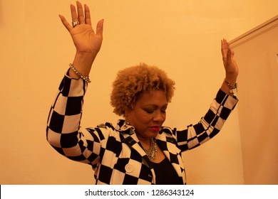 African American Woman In Black And White Checkered Jacket With Hands Raised In Praise And Worship