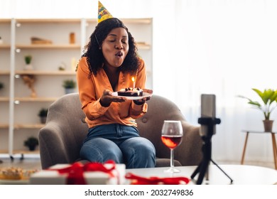 African American Woman Blowing Candle On Birthday Cake In Front Of Cellphone During Online Celebration Of Her B-Day Via Video Call At Home. Virtual Party, Holiday Concept