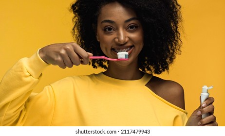 African American Woman With Braces Smiling And Brushing Teeth Isolated On Yellow