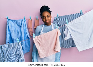 African American Woman With Braided Hair Washing Clothes At Clothesline Depressed And Worry For Distress, Crying Angry And Afraid. Sad Expression. 