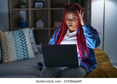 African American Woman With Braided Hair Using Computer Laptop At Night Crazy And Scared With Hands On Head, Afraid And Surprised Of Shock With Open Mouth 