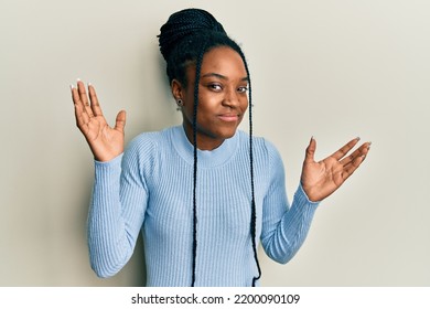African American Woman With Braided Hair Wearing Casual Blue Sweater Clueless And Confused With Open Arms, No Idea And Doubtful Face. 
