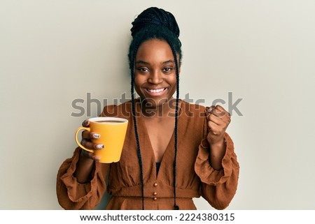 African american woman with braided hair drinking a cup coffee screaming proud, celebrating victory and success very excited with raised arm 