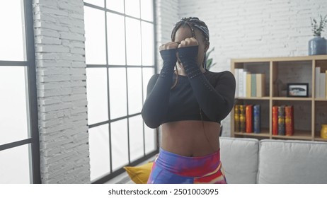 African american woman with braids boxing indoors in a stylish living room, showing fitness and empowerment. - Powered by Shutterstock