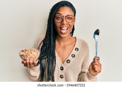 African American Woman With Braids Eating Healthy Whole Grain Cereals Winking Looking At The Camera With Sexy Expression, Cheerful And Happy Face. 