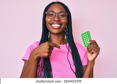 African american woman with braids holding birth control pills pointing finger to one self smiling happy and proud 