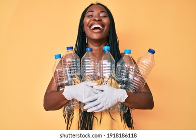 African american woman with braids holding recycling plastic bottles smiling and laughing hard out loud because funny crazy joke. 