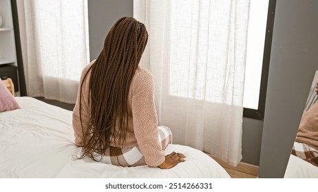 African american woman with braids sitting thoughtfully in a cozy bedroom setting, depicting serenity and introspection. - Powered by Shutterstock