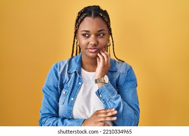 African American Woman With Braids Standing Over Yellow Background Touching Mouth With Hand With Painful Expression Because Of Toothache Or Dental Illness On Teeth. Dentist 