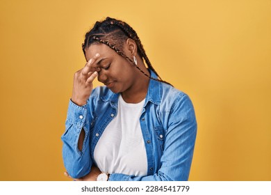 African american woman with braids standing over yellow background tired rubbing nose and eyes feeling fatigue and headache. stress and frustration concept.  - Shutterstock ID 2284541779