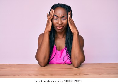 African american woman with braids wearing casual clothes sitting on the table suffering from headache desperate and stressed because pain and migraine. hands on head. 