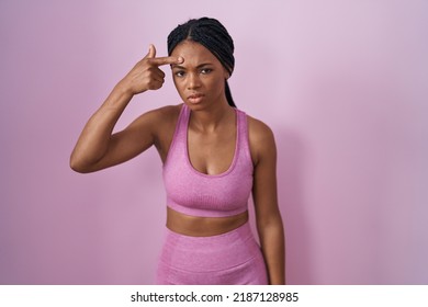African american woman with braids wearing sportswear over pink background pointing unhappy to pimple on forehead, ugly infection of blackhead. acne and skin problem 