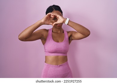 African american woman with braids wearing sportswear over pink background doing heart shape with hand and fingers smiling looking through sign  - Powered by Shutterstock