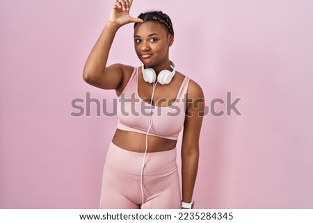 African american woman with braids wearing sportswear and headphones making fun of people with fingers on forehead doing loser gesture mocking and insulting. 