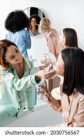 African American Woman Brushing Teeth Near Blurred Friends In Bathroom