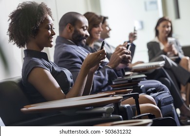 African American Woman Or Businesswoman Texting Using Cell Phone In Busy Airport With Other People Traveling In The Background