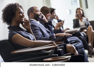 African American Woman Or Businesswoman Using Cell Phone In Busy Airport With Other People In Background