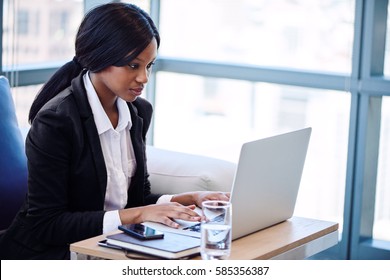 African American Woman Busy Sitting And Typing On Her Notebook While Seated On A Sofa In A Business Lounge In The Airport.