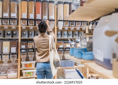 African american woman buying organic cereals and grains in sustainable zero waste grocery store. Young woman refilling reusable container in local grocery store - Powered by Shutterstock