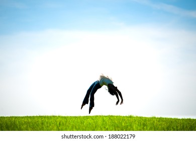 African American Woman Captured In Mid-air Doing A Back Flip In A Fresh Spring Field. Silhouetted.