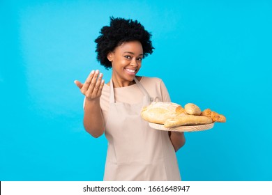 African american woman in chef uniform. Female baker holding a table with several breads inviting to come with hand. Happy that you came