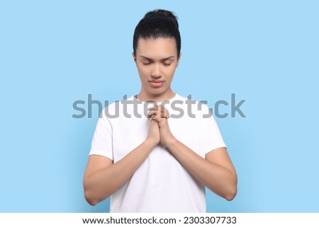 African American woman with clasped hands praying to God on light blue background
