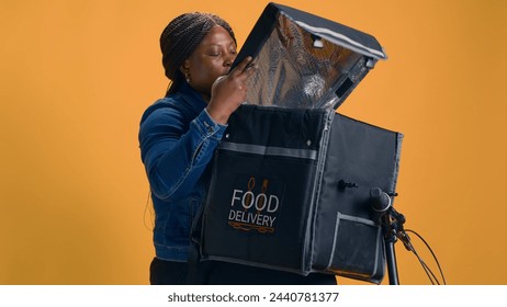 African American woman collecting takeaway from food delivery bag for client. Professional courier provides quick and dependable customer service by delivering delicious takeout meals with bicycle. - Powered by Shutterstock