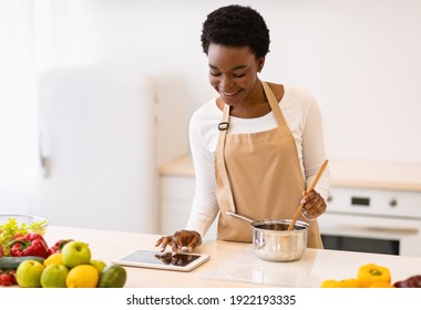 African American Woman Cooking With Digital Tablet Browsing Dinner Recipes Online Standing Wearing Apron In Modern Kitchen Indoors. Healthy Nutrition Application, Food Prepatation Concept