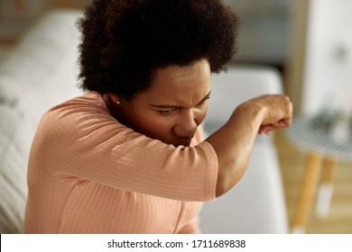 African American woman coughing into her elbow at home. - Powered by Shutterstock