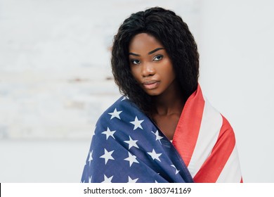 african american woman covered with flag of american looking at camera