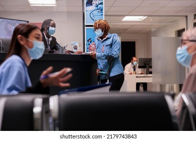 African American Woman With Crutches Talking To Receptionist In Hospital Lobby, Chatting About Medical Appointment And Healthcare. Patient With Physical Impairment At Reception Desk.