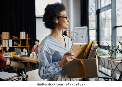 African american woman with curly hair packing her items during lay off, colleagues on backdrop. - Powered by Shutterstock