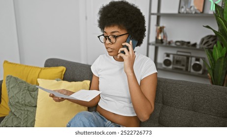 African american woman with curly hair making a phone call and reading a paper in her modern living room. - Powered by Shutterstock