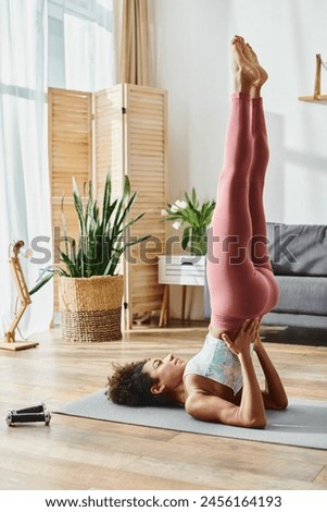 African American woman with curly hair, dressed in activewear, performs a handstand on a yoga mat at home.