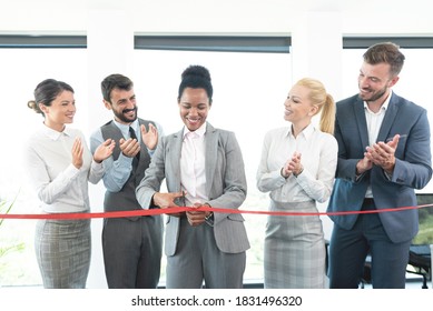 African american woman cutting red ribbon while colleagues are clapping hands at office