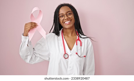 African american woman doctor holding breast cancer awareness pink ribbon over isolated pink background - Powered by Shutterstock