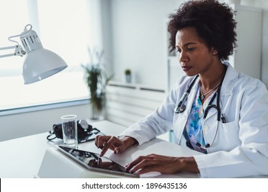 African American Woman Doctor Working At Her Office Online Using Portable Inormation Device. Telemedicine Services. Primary Care Consultations, Psychotherapy, Emergency Services. 