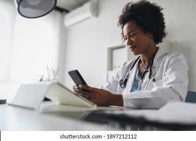 African American Woman Doctor Working At Her Office Online Using Portable Inormation Device. Telemedicine Services. Primary Care Consultations, Psychotherapy, Emergency Services. 