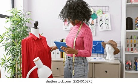 African american woman dressmaker using tablet in a tailor shop surrounded by sewing items and mannequins. - Powered by Shutterstock