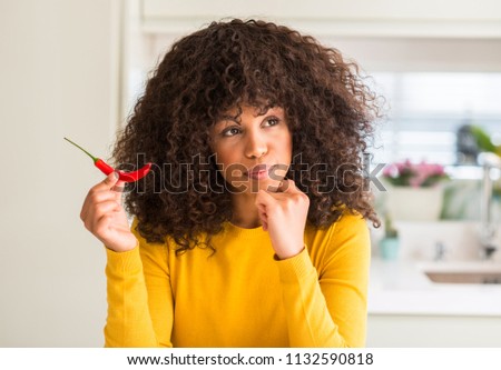 African american woman eating red hot chili pepper serious face thinking about question, very confused idea