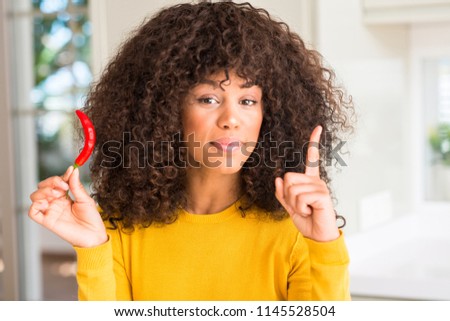 African american woman eating red hot chili pepper surprised with an idea or question pointing finger with happy face, number one