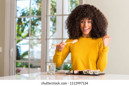 African american woman eating sushi using chopsticks at home screaming proud and celebrating victory and success very excited, cheering emotion
