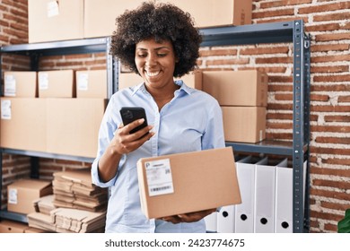 African american woman ecommerce business worker using smartphone holding package at office - Powered by Shutterstock