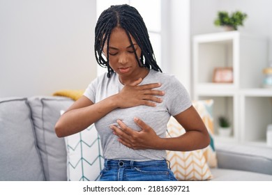 African american woman examining breast sitting on sofa at home