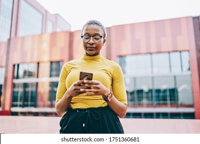 African American woman in eyeglasses with modern smartphone checking mail on device using 4G internet connection at urban setting, dark skinned female reading received sms message on cellular - Powered by Shutterstock