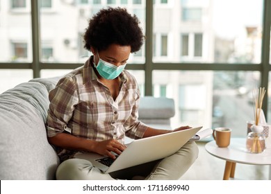 African American Woman With Face Mask Working On Laptop In Her Living Room.