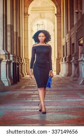 African American Woman Fashion In New York. Wearing Long Sleeve, Slim, Off Shoulder Dress, Carrying Blue Bag, Young Lady Walking On Vintage Style, Narrow Street, Going To Work. Instagram Effect. 