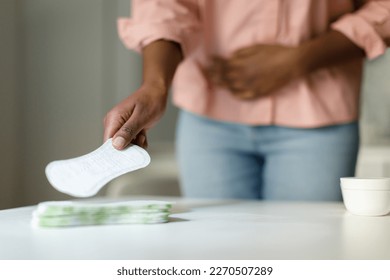 African american woman feeling pain during menstrual cycle and taking daily sanitary pad from table, selective focus, closeup, free space - Shutterstock ID 2270507289