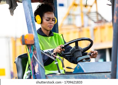 African American Woman Forklift Driver Operator Driving Vehicle Wearing Safety  Hard Hat At Cargo Warehouse And Container Yard. Logistic And Marine Concept