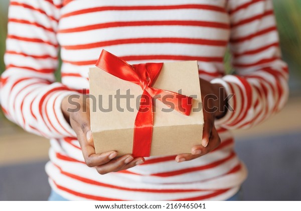 african American woman gives or receives a gift. a\
happy millennial woman with a cardboard box and a red ribbon in her\
hands. an anniversary and birthday gift for a friend or wife. party\
joy and